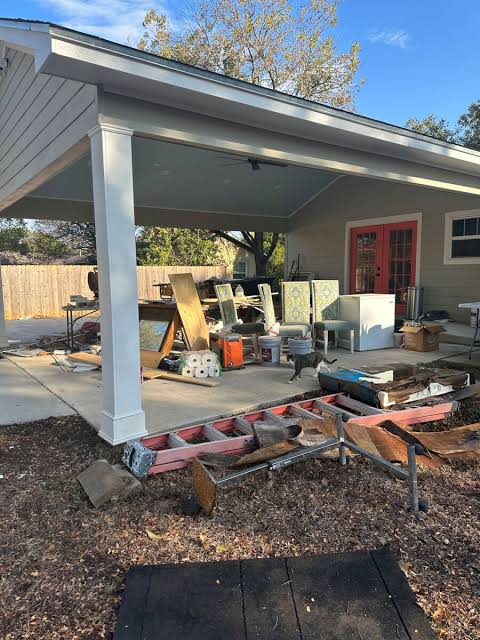 Original covered patio filled with construction materials, furniture, tools, and clutter